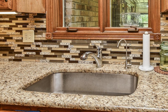 interior details featuring light stone countertops, brown cabinetry, a sink, and backsplash
