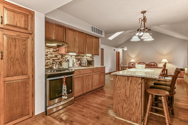 kitchen featuring under cabinet range hood, wood finished floors, visible vents, stainless steel range, and a breakfast bar area