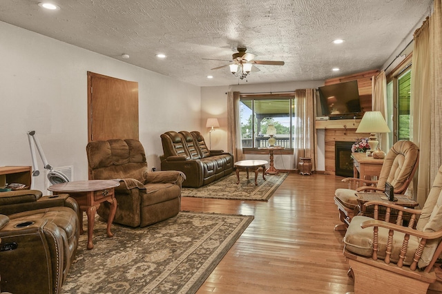 living area featuring a fireplace, a textured ceiling, light wood-style floors, and ceiling fan