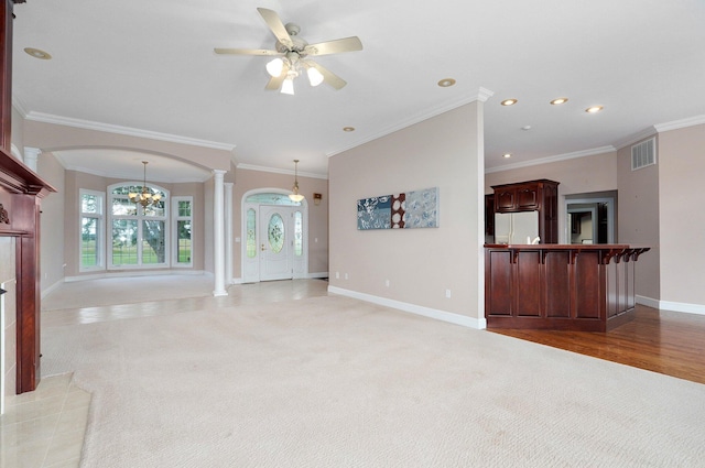 unfurnished living room featuring ornate columns, ceiling fan with notable chandelier, crown molding, and carpet flooring