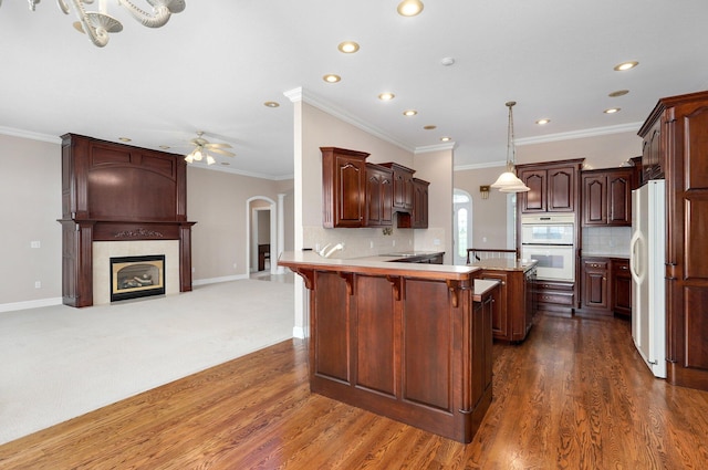 kitchen with ornamental molding, kitchen peninsula, white appliances, and dark hardwood / wood-style flooring