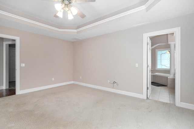 unfurnished bedroom featuring ceiling fan, a raised ceiling, connected bathroom, light colored carpet, and ornate columns