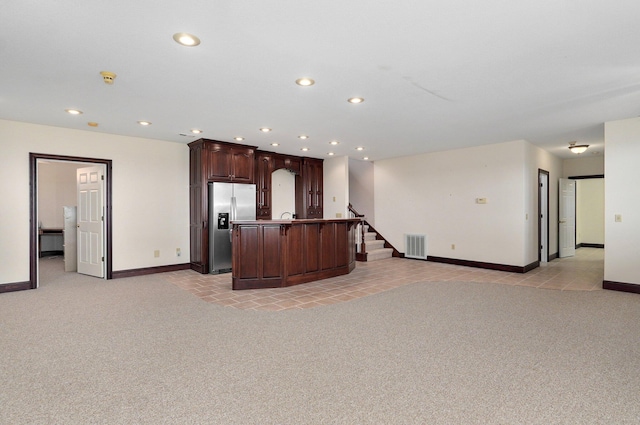 kitchen with dark brown cabinets, stainless steel refrigerator with ice dispenser, a kitchen island with sink, and light carpet