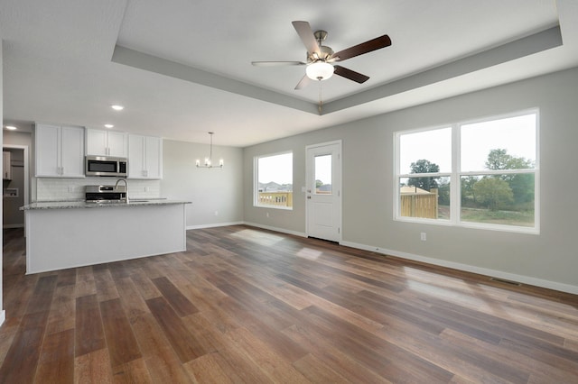 unfurnished living room featuring ceiling fan with notable chandelier, dark hardwood / wood-style floors, and a raised ceiling