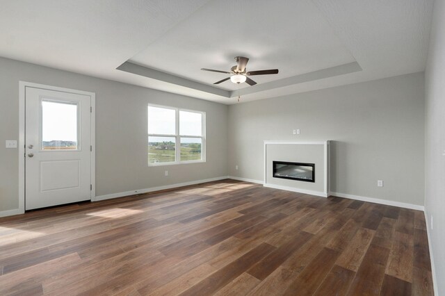 unfurnished living room featuring ceiling fan, a wealth of natural light, a tray ceiling, and dark hardwood / wood-style floors