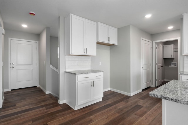 kitchen with tasteful backsplash, light stone countertops, dark hardwood / wood-style flooring, and white cabinetry