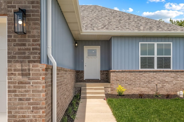 view of exterior entry featuring brick siding and roof with shingles