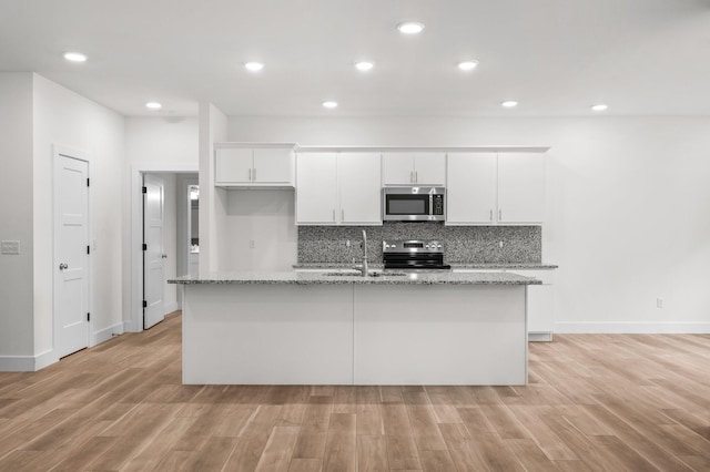 kitchen with appliances with stainless steel finishes, light wood-type flooring, a kitchen island with sink, and white cabinetry