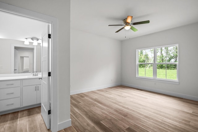 empty room with light wood-type flooring, a ceiling fan, baseboards, and a sink