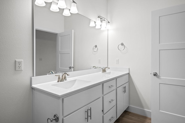 bathroom with baseboards, wood finished floors, a sink, and double vanity