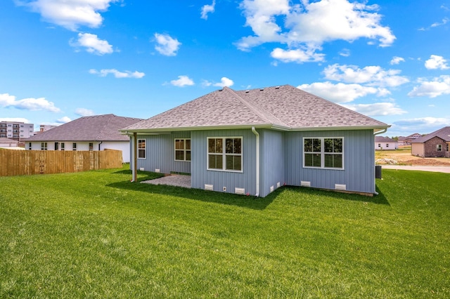 back of property with roof with shingles, fence, and a lawn