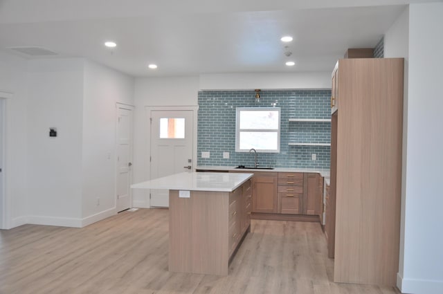 kitchen with a kitchen island, sink, light wood-type flooring, and decorative backsplash