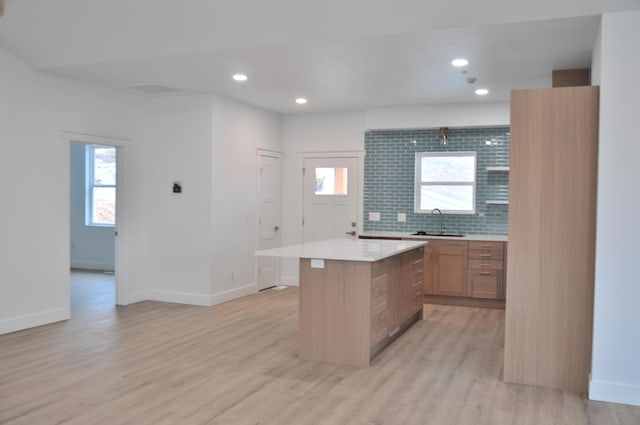 kitchen featuring a kitchen island, sink, light wood-type flooring, and decorative backsplash