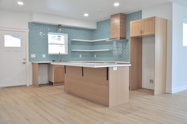 kitchen featuring sink, light hardwood / wood-style floors, a kitchen island, decorative backsplash, and wall chimney exhaust hood