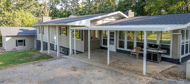 rear view of house with a patio area, a chimney, aphalt driveway, a carport, and a sunroom