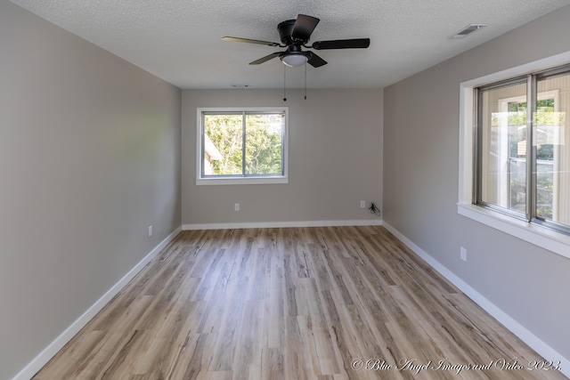 empty room with a textured ceiling, ceiling fan, light wood-style flooring, baseboards, and visible vents