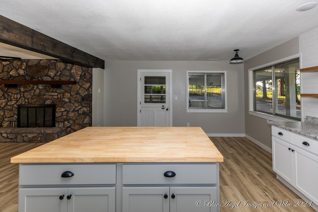 kitchen featuring light wood-type flooring, tasteful backsplash, white cabinets, butcher block counters, and a fireplace