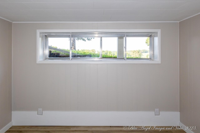 empty room with ornamental molding, wooden walls, a wealth of natural light, and wood-type flooring