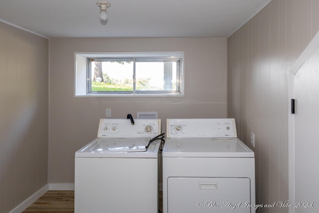 clothes washing area featuring hardwood / wood-style flooring, wood walls, and washing machine and clothes dryer