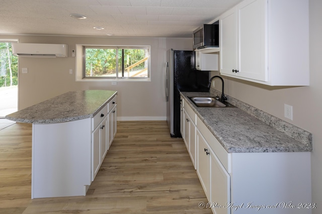 kitchen with light wood finished floors, an AC wall unit, a sink, and white cabinets