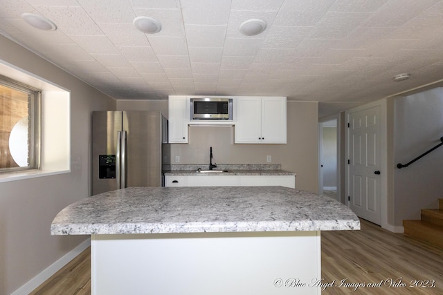 kitchen featuring wood finished floors, a sink, stainless steel appliances, white cabinets, and baseboards