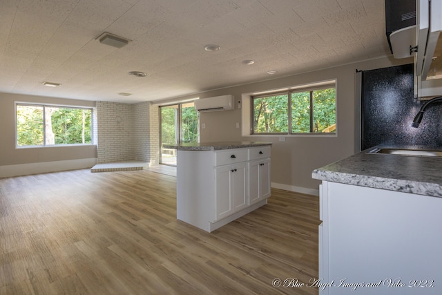 kitchen with plenty of natural light, white cabinets, a wall unit AC, and sink