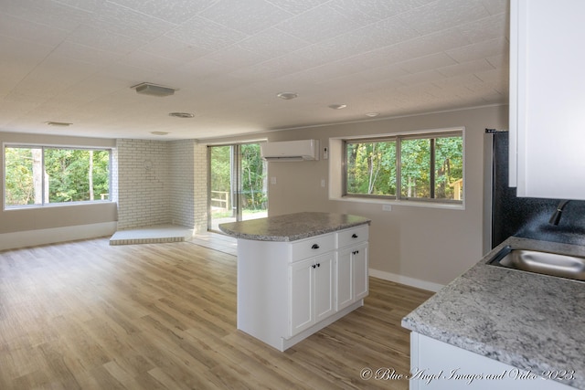 kitchen featuring light wood-type flooring, light stone counters, a kitchen island, white cabinets, and a wall mounted AC