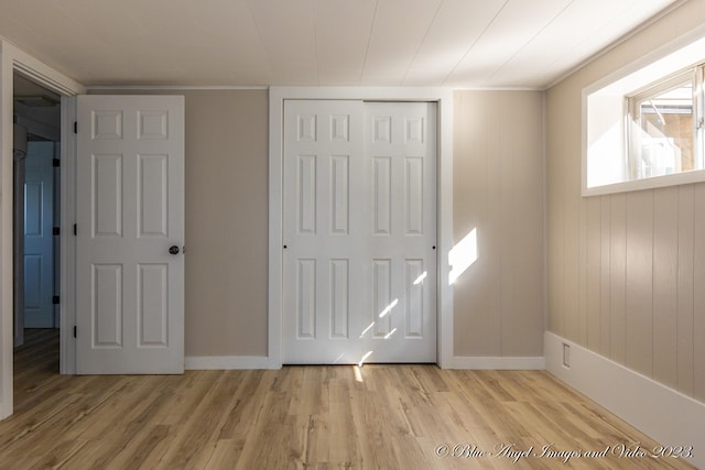 unfurnished bedroom with light wood-type flooring, wooden walls, and a closet