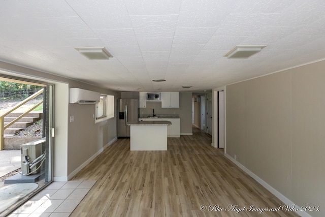 kitchen featuring a kitchen island, white cabinetry, stainless steel appliances, light wood-type flooring, and an AC wall unit