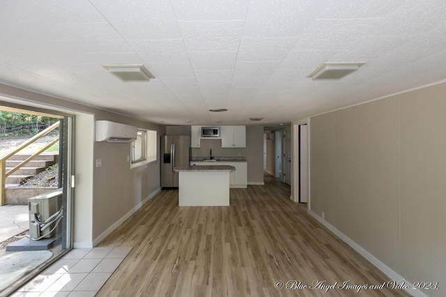 kitchen featuring a wall mounted air conditioner, light wood-style floors, stainless steel appliances, white cabinetry, and a kitchen island