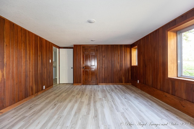 unfurnished room with wooden walls, a healthy amount of sunlight, and light wood finished floors