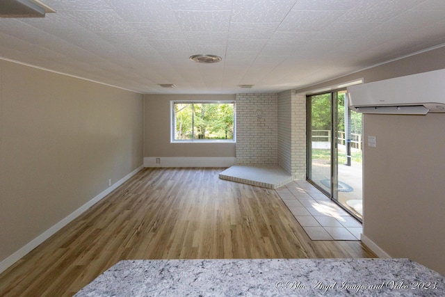 spare room featuring baseboards, wood finished floors, a wall mounted AC, and plenty of natural light