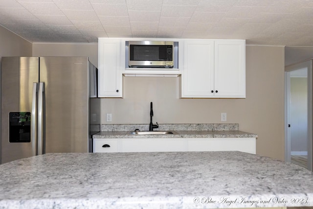 kitchen with stainless steel appliances, a sink, white cabinetry, and light stone counters