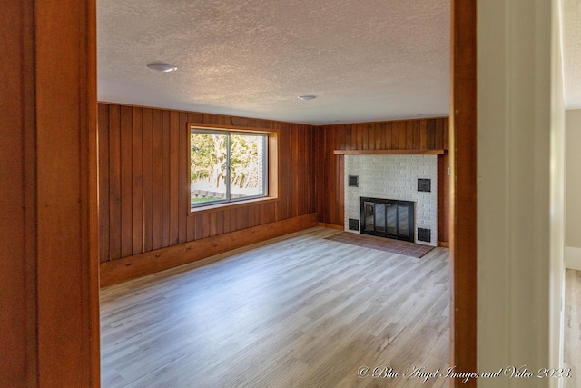unfurnished living room with a fireplace, light wood-style flooring, a textured ceiling, and wood walls