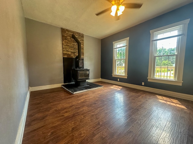 unfurnished living room featuring ceiling fan, dark hardwood / wood-style flooring, vaulted ceiling, a wood stove, and a textured ceiling