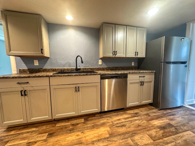 kitchen with dark stone countertops, stainless steel appliances, sink, and light hardwood / wood-style flooring