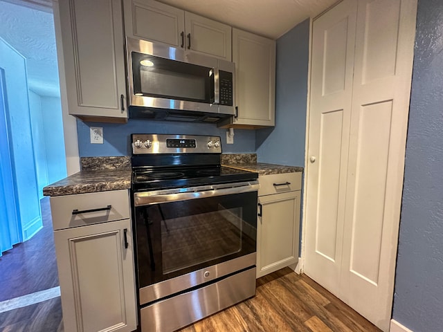 kitchen featuring appliances with stainless steel finishes, dark wood-type flooring, and dark stone counters