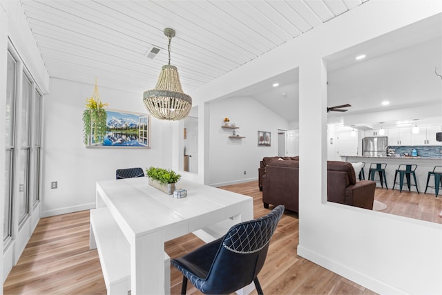 dining space with an inviting chandelier, light hardwood / wood-style flooring, and vaulted ceiling