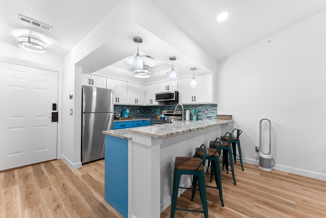 kitchen with appliances with stainless steel finishes, backsplash, light hardwood / wood-style floors, and white cabinetry