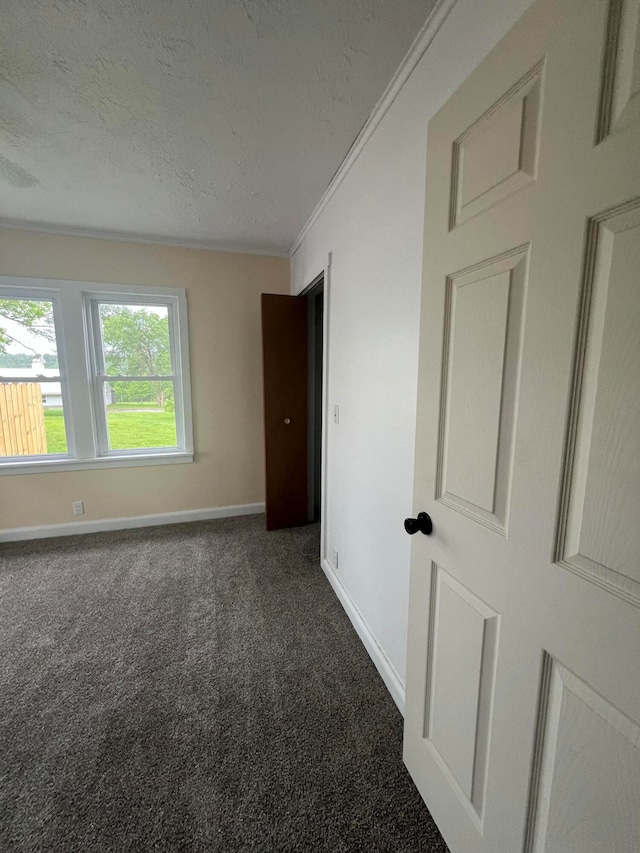 spare room with crown molding, dark carpet, and a textured ceiling