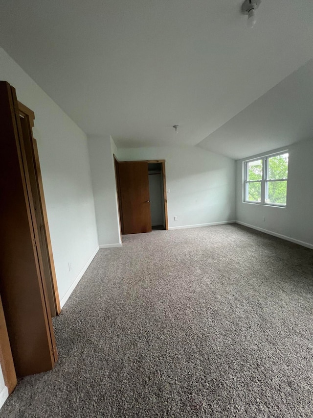 empty room with vaulted ceiling and dark colored carpet