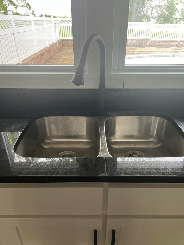 details with dark stone counters, white cabinetry, and sink