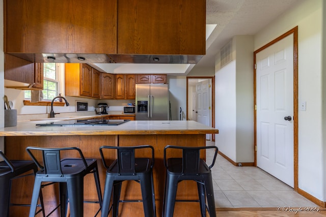 kitchen featuring light tile patterned floors, sink, kitchen peninsula, stainless steel refrigerator with ice dispenser, and a kitchen bar