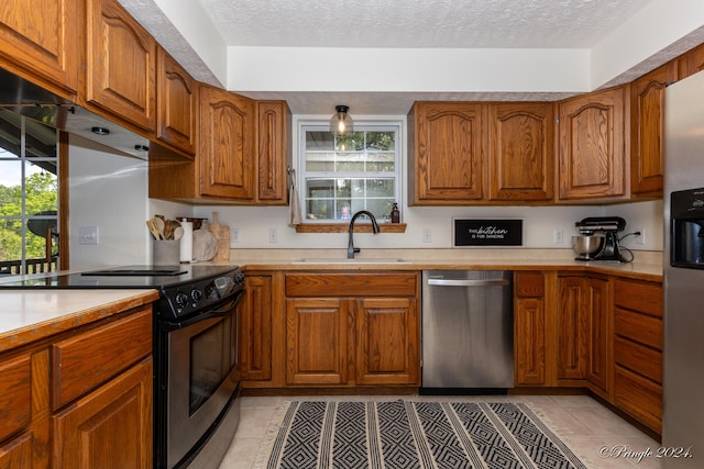 kitchen featuring stainless steel appliances, light countertops, a sink, and brown cabinetry