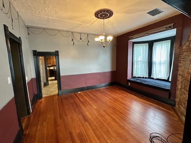 624 S Ash St, Nevada, MO 64772 - unfurnished dining area with an inviting chandelier, wood finished floors, visible vents, and baseboards