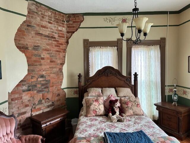 bedroom featuring crown molding, an inviting chandelier, and brick wall