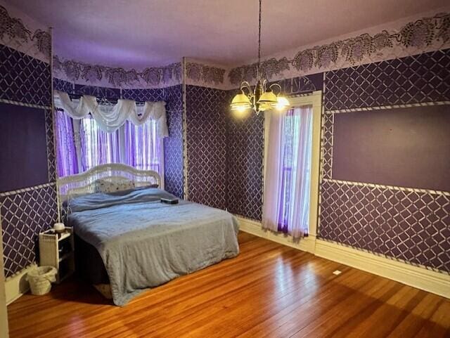624 S Ash St, Nevada, MO 64772 - bedroom with baseboards, wood finished floors, an inviting chandelier, and wallpapered walls
