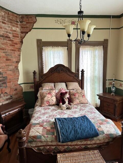 bedroom featuring brick wall, hardwood / wood-style floors, a chandelier, and multiple windows