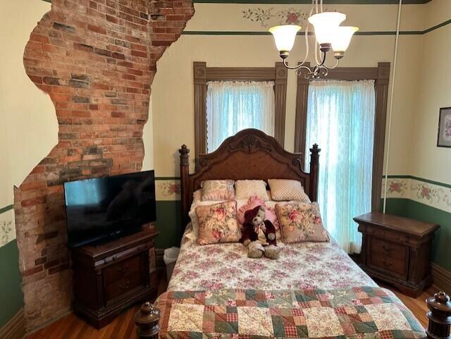 bedroom featuring an inviting chandelier, brick wall, and hardwood / wood-style flooring