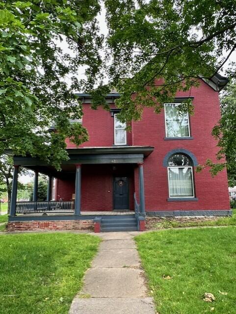 624 S Ash St, Nevada, MO 64772 - view of front facade with brick siding, a porch, and a front lawn